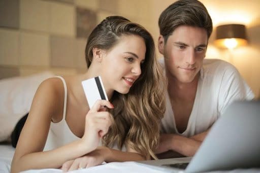 A cheerful couple in bed, making online purchases on a laptop.